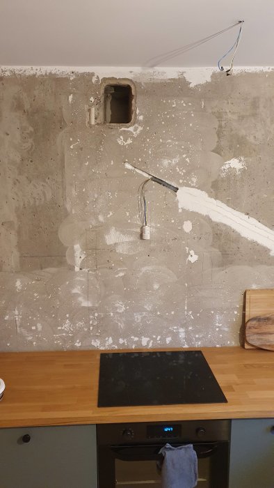 Murad vägg i kök med äldre ventilationshål ovanför spis, vit kabel hänger och spackelarbeten syns.