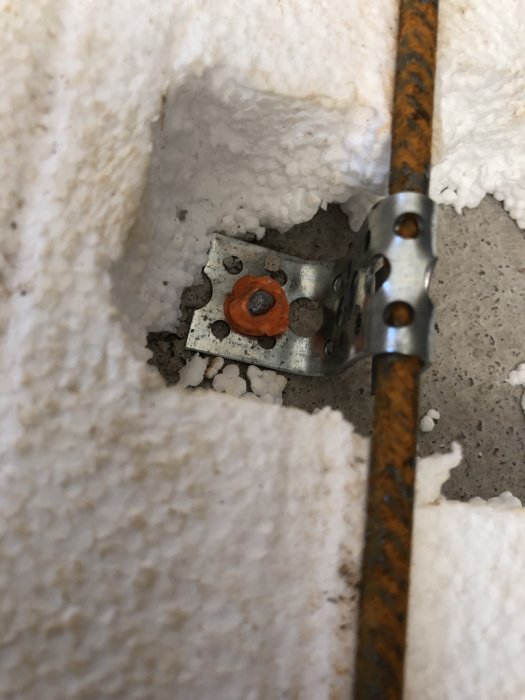 Monteringsdetalj som används för att fästa armeringsjärn, med orange plastbricka, på betongyta omgiven av isoleringsskum.
