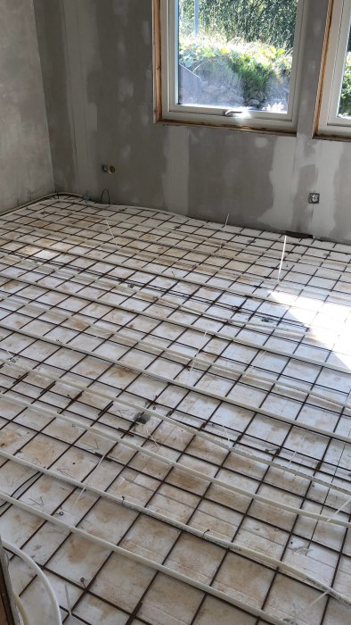 Ett tomt rum under renovering med armeringsnät utlagt på golvet före betonggjutning.
