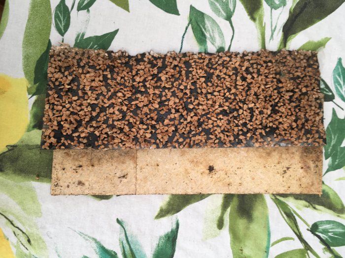 Del av ett gammalt golvspån med en svart matta ovanpå placerad på ett mönstrat underlag.