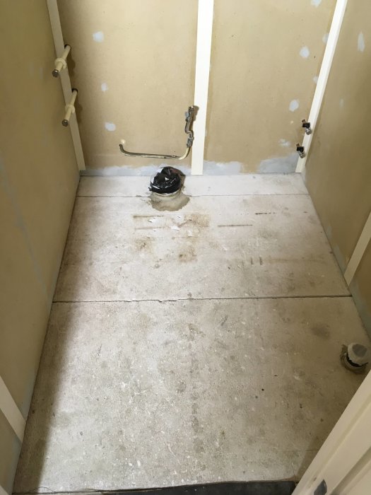 Rivna golvspån och svart matta synlig vid avlopp i renoveringsprojekt av toalett.