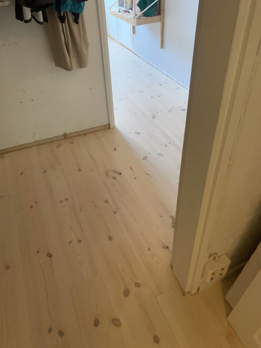 Nyinstallerat trägolv som sträcker sig från en hall in i ett barnrum, med detalj av skärningen runt dörrposten.