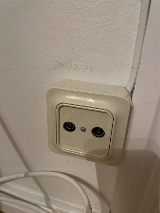 Vägguttag för TV-antennkabel, inte ansluten, på en vit vägg.