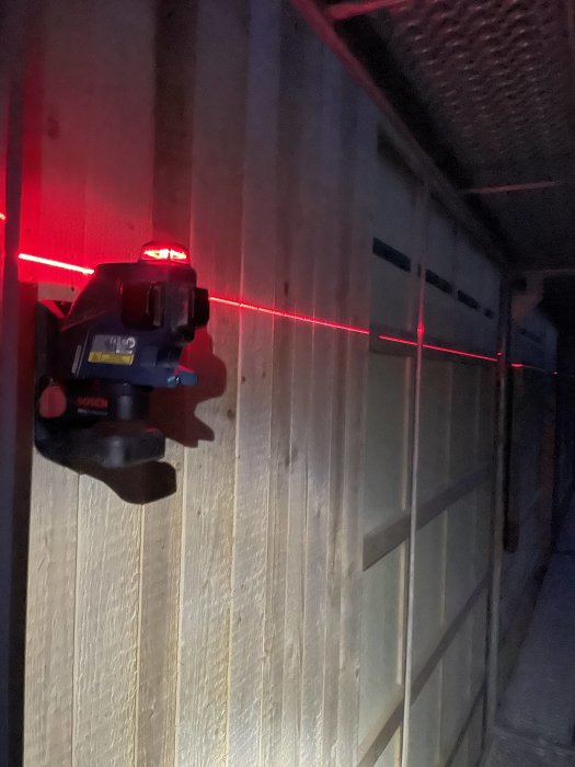 Ramsågad granpanel med laserlinje som markerar spiklinje, fastsatt med fasadspik och något suddig bakgrund.