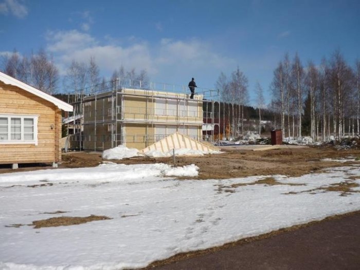 Gavelspetsar på marken framför konstruktion med byggnadsställningar och smältande snö.