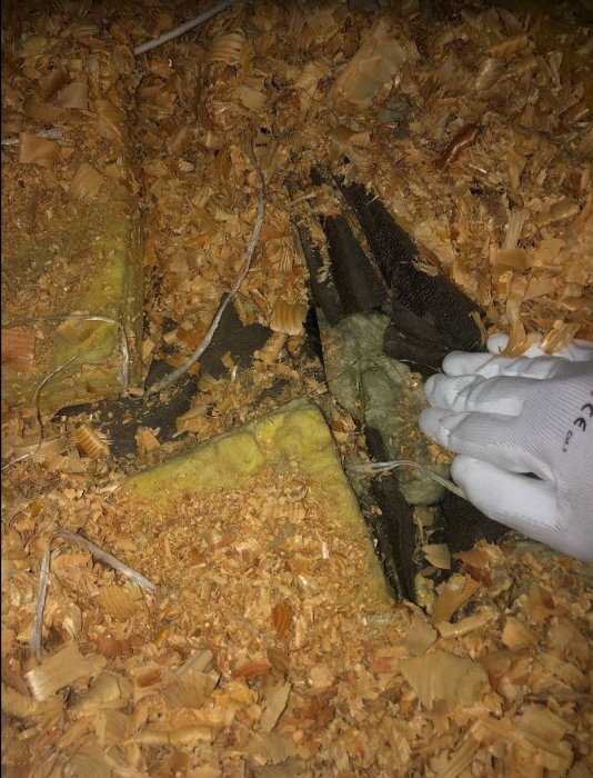 Röra av olika isoleringsmaterial i ett vindutrymme, inkluderar sågspån och gamla isoleringsmattor.