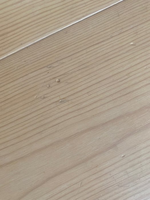Slitet vitvaxat furugolv med synliga nötningsspår och små fläckar.