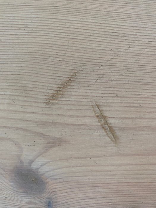 Närbild av slitet vitvaxat furugolv med synliga repor och en mörk kvist.