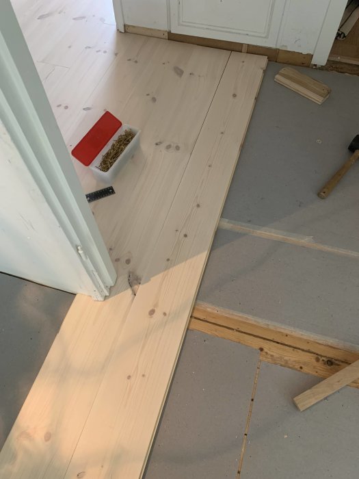 Installation av trägolv med golvbrädor som delvis lagts nära en dörrkarm, verktyg i närheten.