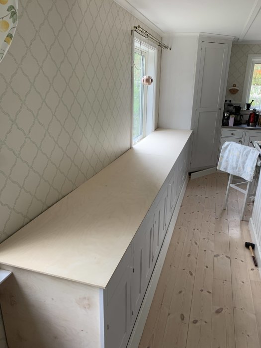 Kök med nyligen installerade grå underskåp och temporära arbetsbänkar i plywood.