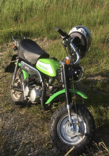 Grön Kawasaki minibike parkerad på en äng i solljus.