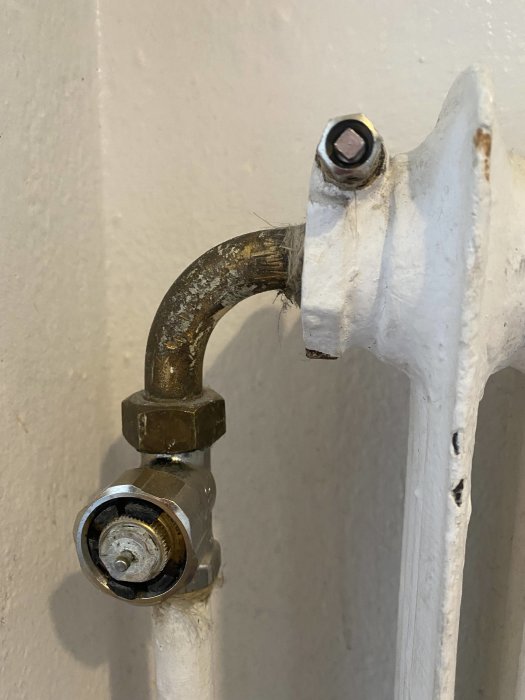 Avstängningsventil och en avlägsnad termostat på en radiator, med synliga rör och skador på termostatfästet.