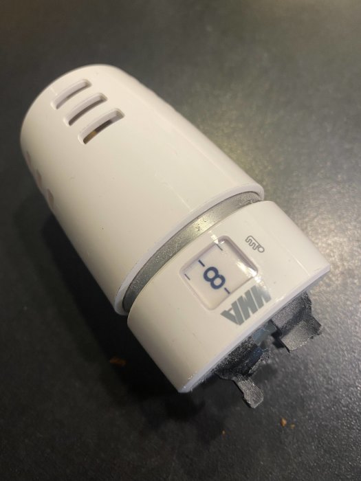 En trasig vit radiator termostat med spruckna plastdelar på en svart yta.
