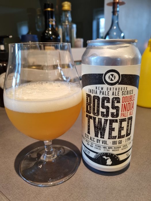 Ett glas fyllt med öl bredvid en ölburk på en köksbänk.