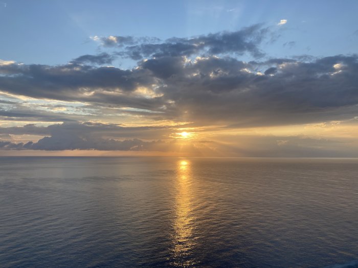 Solnedgång över havet med solstrålar som bryter genom molnen och reflekterar i vattnet.