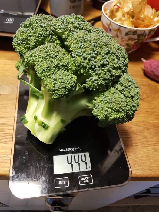 Broccoliplanta som väger 444 gram på en digital köksvåg.