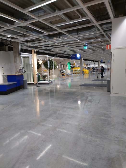 Interiör av en stor butik med högt i tak, exponerade luftkanaler och kund som går med kundvagn.