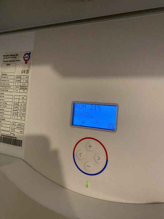 Värmepumpsdisplay som visar rumstemperatur på 21 grader och automatläge aktiverat, intill kontrollpanel.