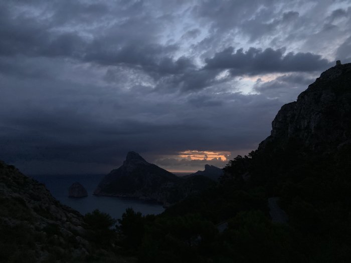 Tidig morgon med utsikt över havet, berg och en solnedgång mellan molnen.