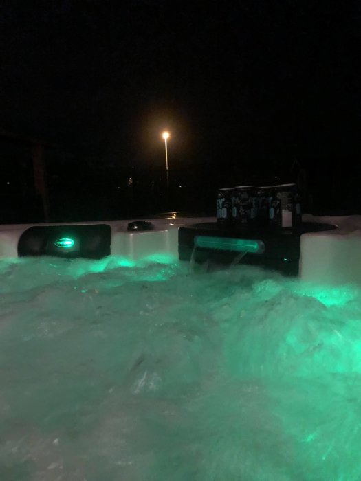 Uppvärmt bubbelbad utomhus med grönt ljus på natten, gatlykta i bakgrunden.