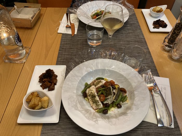 Middagsdukning med tallrik med grillade grönsaker och kyckling, sidorätter, glas vin och vattenflaska.