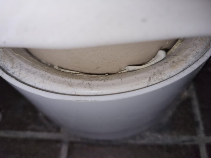 Anslutning för en toalettstol med synlig brun fogmassa runt avloppsröret.