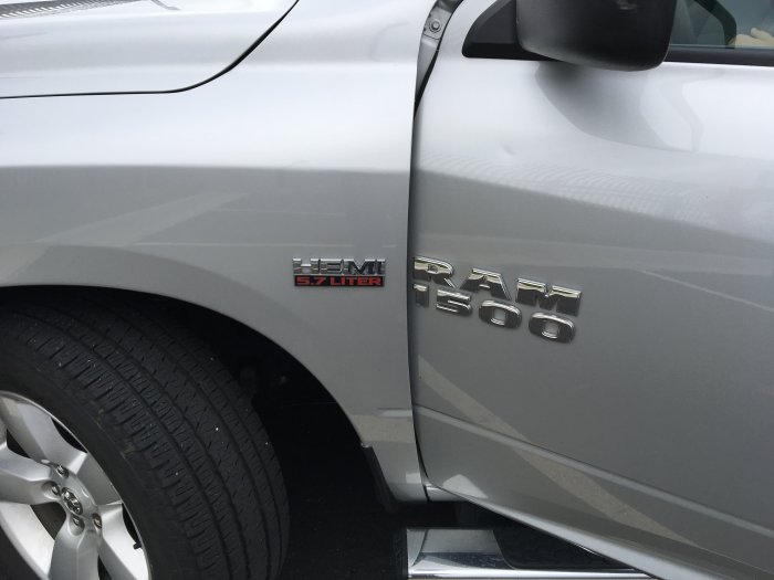 Detaljbild på sidan av en silverfärgad pickup visande dekaltrim med "HEMI 5.7 LITER" och "RAM 1500" loggor.