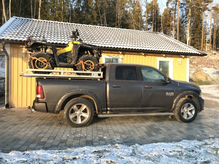 Pickup med två fyrhjulingar monterade på flaket framför en byggnad.