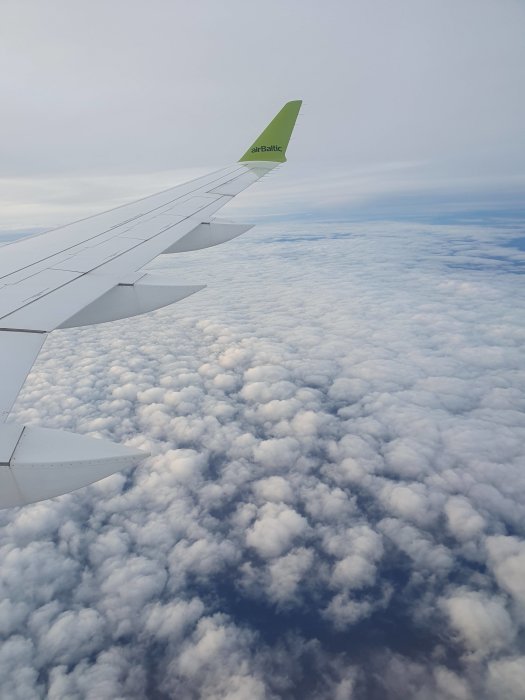 Flygplansvinge med flygbolagets logotyp över molntäcke sett från flygplansfönster.