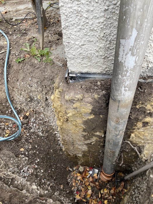 Uppgrävd hörna av ett hus med synlig grund och gammal tegelrör, misstänkt fuktskada och dräneringsfrågor.