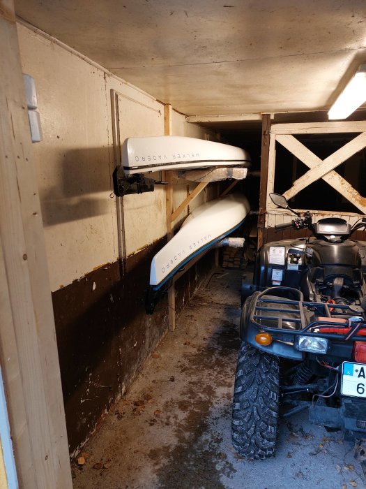 Två vita kajaker förvarade på höjden i ett garage med en ATV parkerad under dem.