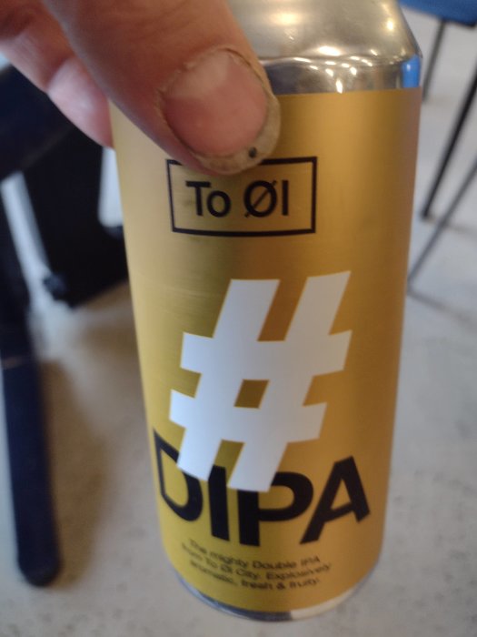 Hand håller en burk öl märkt 'To Øl DIPA' med suddig bakgrund.