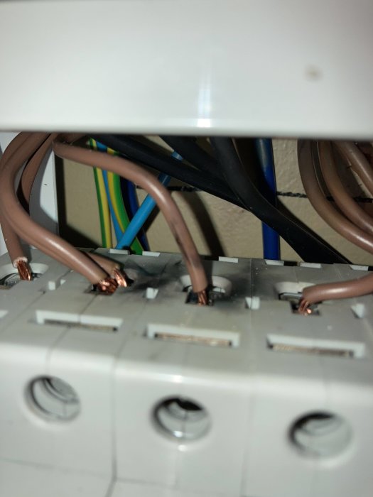 Närbild på säkringar i elcentral med synliga svetsmärken och skadade kablar.