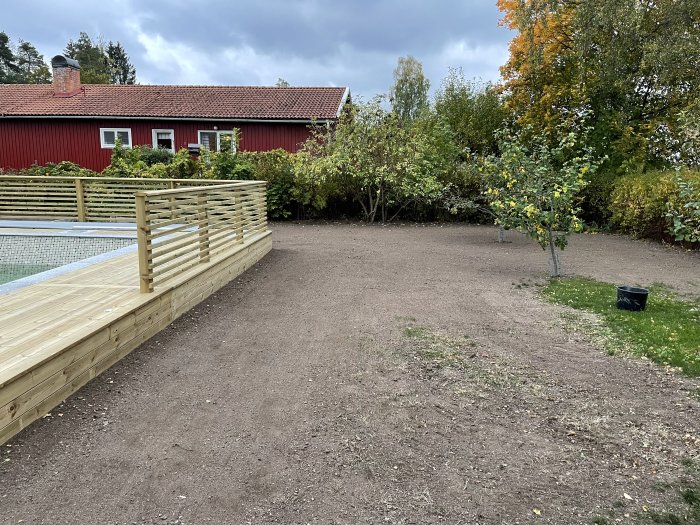 Nyplanerad jord och en pool med trätrall framför ett rött hus omgivet av träd i höstfärger.