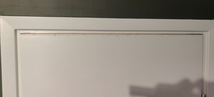 Dörröverkant med synliga skruvhål och slitage efter justering av gångjärn.