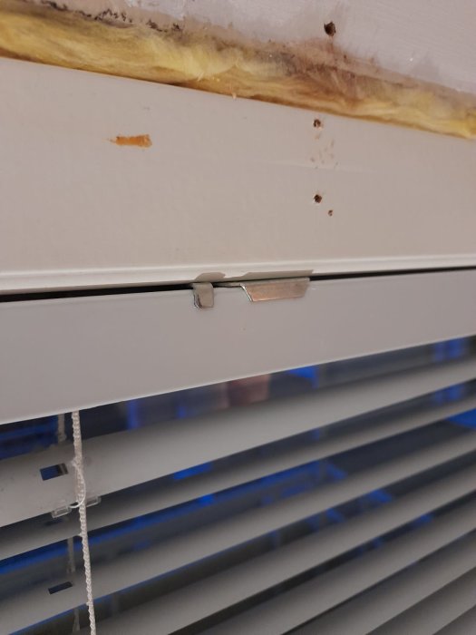 Metallfäste på persienn vid fönsterkarm som verkar svårt att demontera.
