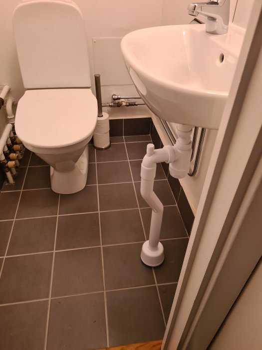 Gästtoalett med nyinstallation av handfat nära WC, synliga rör som sticker ut mot toaletten.