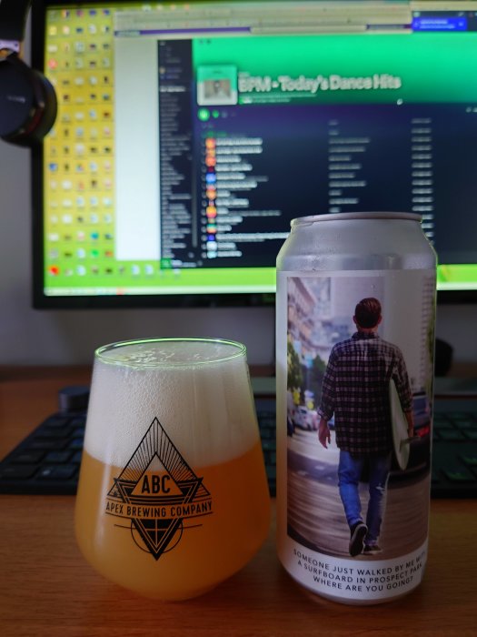 Ölglas med skum och burk med bild av person som går, framför datorskärm med musikspelare.