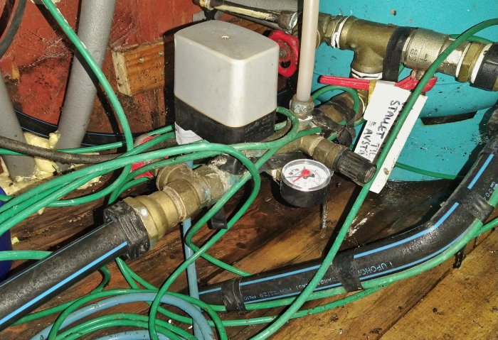 Vattenpump och tryckströmbrytare med sladdar och rörinstallationer i ett pumprum.
