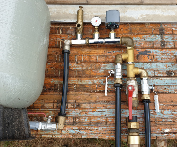 Vatteninstallation med röd kulventil, backventil, PEM-slangar, tryckströmbrytare, manometer och säkerhetsventil monterade på vägg.