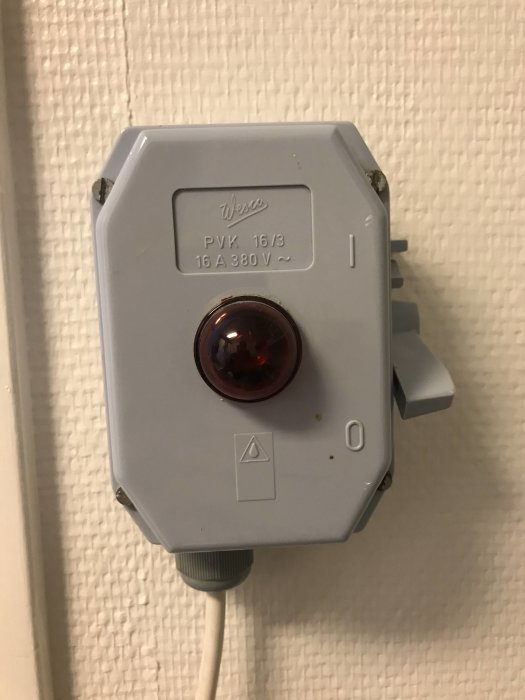 En fast installerad vägguttag för 380V med en röd indikatorlampa och ansluten kabel.