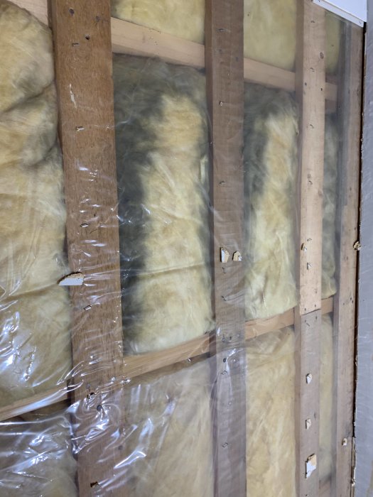 Isoleringsmaterial mellan träreglar med synliga mörka områden som kan vara mögel eller smuts.