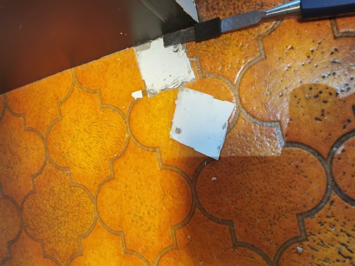 Bitar av orange plast- och heltäckningsmatta med brytjärn och gulbrunt lim på betong.