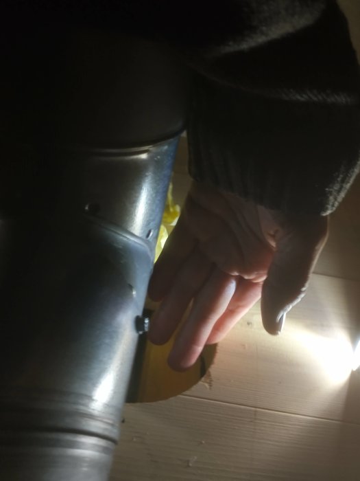 Hand som visar ett stort glapp mellan ett ventilationssrör och en träpanel i ett tak.