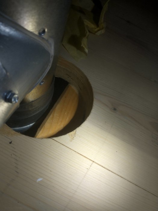 Ventilationsrör som går genom ett för stort utskuret hål i ett trägolv.