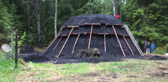 Stor kolmila i skogsmiljö under konstruktion med personer i bakgrunden.