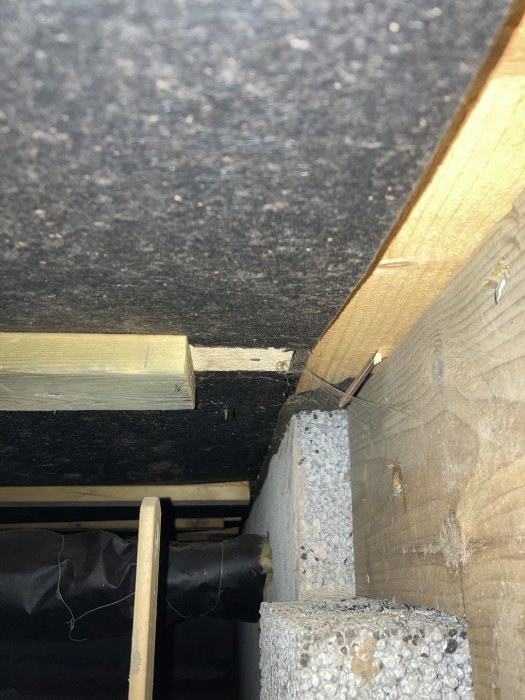 Vy underifrån ett golvbjälklag med synliga träbjälkar, isolering och betongfundament i ett hus.