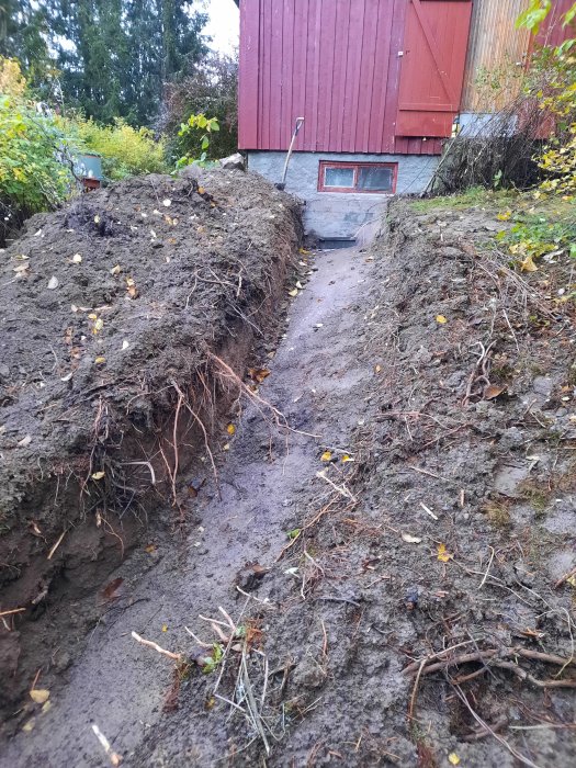 Grävd schakt i trädgården där berg möter jord, framför en röd trävilla med målet att ansluta till kommunalt avlopp.