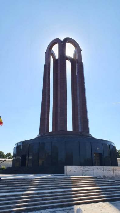 Ståtligt monument med tre bågformade pelare mot en klarblå himmel, klättrat av vita trappsteg i förgrunden.