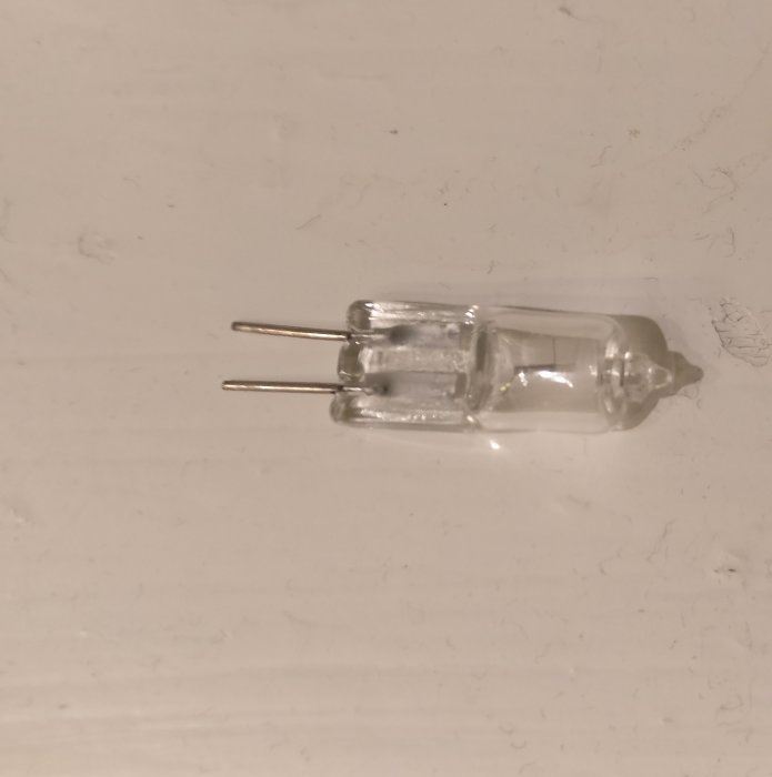 Halogenlampa med två stift för infälld spot, utan skyddslock, liggande på en vit yta.
